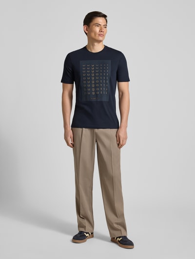 Männermodel trägt Regular Fit T-Shirt mit Logo-Print von bugatti in Dunkelblau, Reine Baumwolle, Rundhalsausschnitt, Rückenlänge Größe M 70 cm, Ganzkörperansicht von vorne.