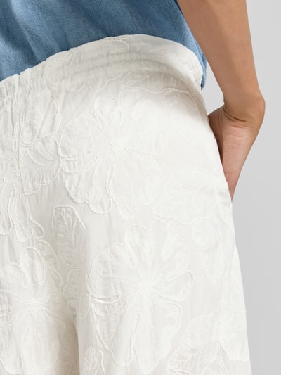 Frauenmodel trägt Wide Fit Stoffhose mit floralem Allover-Design von Mango, Reine Baumwolle, weiß, strukturierte Oberfläche, Nahaufnahme Hüfte.