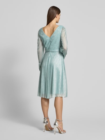 Modelka nosi Regular Fit Kleid in Wickel-Optik von TROYDEN COLLECTION, błyszcząca siateczka, dekolt w serek, długość tyłu 90 cm, długość rękawów 67 cm, wszyty zamek błyskawiczny, kolor jasnomiętowy, kopertowy styl, całopostaciowy widok z tyłu.