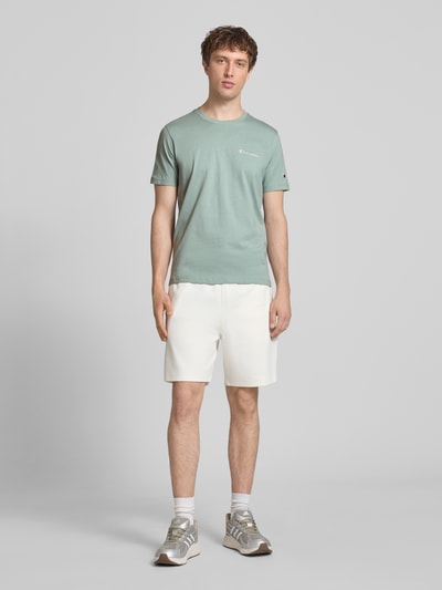 Männermodel trägt T-Shirt mit Label-Stitchings und Rundhalsausschnitt von CHAMPION, grün, reine Baumwolle, Regular Fit, Ganzkörperansicht von vorne.