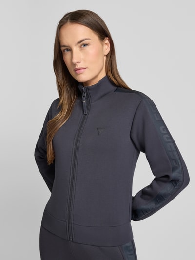 Frauenmodel trägt Regular Fit Sweatjacke aus Viskose-Mix von Guess, dunkelgrau, Stehkragen, Reißverschluss, Logo, Nahaufnahme Oberkörper.
