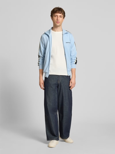 Männermodel trägt Herren Sweatjacke mit Stehkragen Modell 'COTEDAZUR' von Jack & Jones, Slim-Fit, hellblaue Farbe, Reißverschluss, Label-Stitching, Rückenlänge 70 cm, Ärmellänge 65 cm, Ganzkörperansicht von vorne.