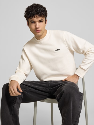 Mężczyznamodel nosi Sweatshirt mit Rundhalsausschnitt und Label-Stitching od Ellesse, bawełniany miks, krój regular fit, kolor ecru, detal z logo, widok na górną część ciała z przodu