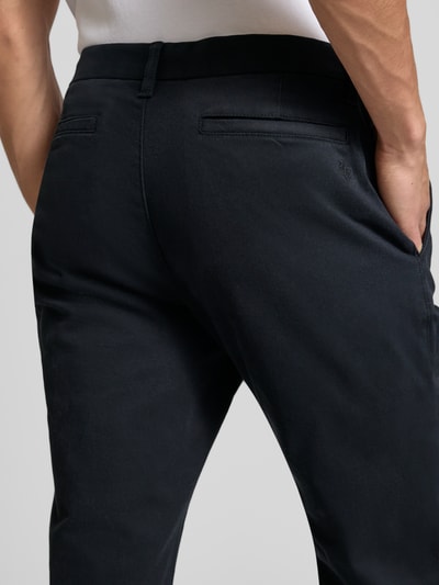 Mężczyzna nosi Schmale Chino mit gerader Silhouette und mittlerer Bundhöhe od REVIEW, bawełna z domieszką elastanu, krój slim fit, średni stan, tylne kieszenie, szerokość w rozmiarze M: 43 cm, długość nogawki wewnętrznej w rozmiarze M: 81 cm, widok z tyłu, zbliżenie na biodra.