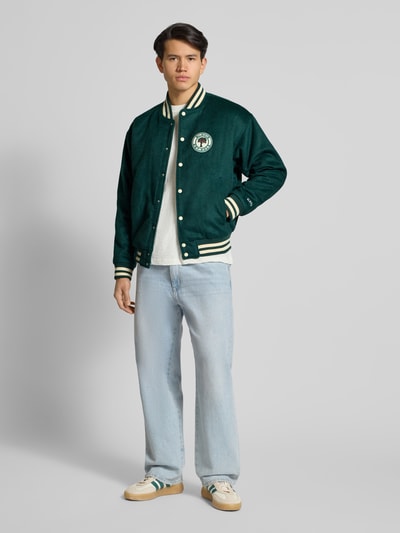 Mannelijk model draagt Regular Fit College Jacke mit Woll-Anteil van BLKVIS, groene stof, label-patch, wit-groene details, vooraanzicht, ganzkörperansicht van voren.