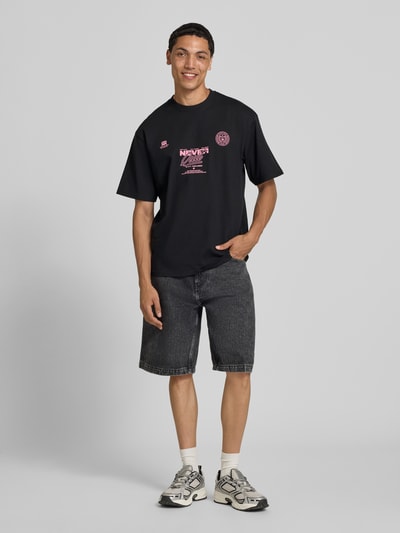 Männermodel trägt T-Shirt mit Statement-Print und Rundhalsausschnitt von Redefined Rebel, Schwarz, Baumwoll-Mix, Relaxed-Fit, Ganzkörperansicht von vorne, Rückenlänge bei Größe M 70 cm.