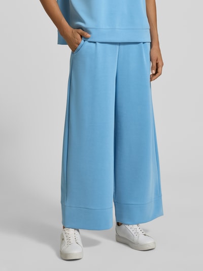 Frauenmodel trägt Wide Leg Sweatpants aus Modal-Mix von Rich & Royal in Hellblau, mit Bundfalten und Taschen, Nahaufnahme Unterkörper. Damen Sweatpants, elastischer Bund, glatte Textur.