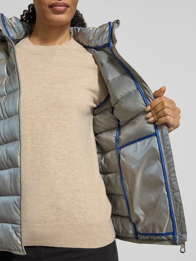 Kobiece model prezentuje Jacke mit Kapuze od NAUTGÅRD w luźnym kroju, z kapturem, tunelem, zakrytym zamkiem, detalem z logo i paskiem na rękawie, długość tyłu w rozmiarze M: 90 cm, szerokość ramion w rozmiarze M: 45 cm, szerokość klatki piersiowej w rozmiarze M: 56 cm, długość rękawa w rozmiarze M: 60 cm, srebrno-beżowe odcienie, miękka tekstura, widoczna wewnętrzna część kurtki, półzbliżenie korpusu z przodu