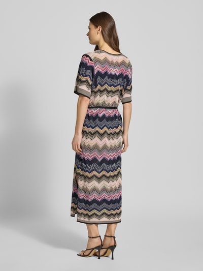 Frauenmodel trägt Strickkleid aus Viskose-Mix mit Bindegürtel von Oui, bunt gemustert, gerader Schnitt, Midikleid, Rückansicht, Ganzkörperansicht.