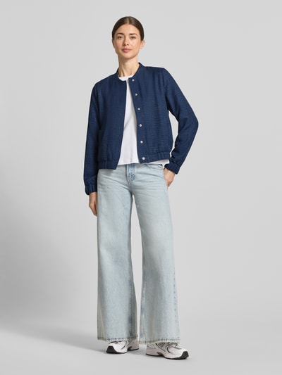 Modelka nosi Regular Fit Blouson mit Baseball-Kragen Modell 'MELANEY' od Vero Moda, melanżowy, długie rękawy, krój regular fit, białe sneakersy, jasne dżinsy, widok całej sylwetki z przodu.
