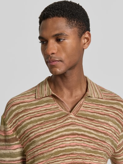Männermodel trägt Relaxed Fit Poloshirt aus reiner Baumwolle Modell 'Muse' von SELECTED HOMME, Optik: Allover-Muster, gestreift, Strick, Farbtöne in Beige, Rosa und Khaki, Nahaufnahme Oberkörper.