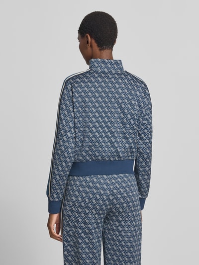 Frauenmodel trägt Regular Fit Sweatjacke mit Allover-Logo-Print von GUESS, blaues Muster, elastische Abschlüsse, Ganzkörperansicht Rückansicht.