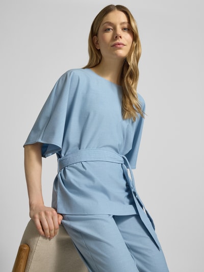 Frauenmodel trägt Relaxed Fit Bluse aus Viskose-Mix Modell 'Rikas' von MOS MOSH in Hellblau mit abnehmbarem Stoffband, Halbarm, Rundhalsausschnitt, Ganzkörperansicht von vorne, Rückenlänge bei Größe S: 63 cm, Ärmellänge bei Größe S: 28 cm.