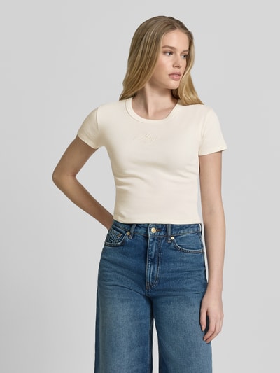 Modelka kobieca nosi Slim Fit T-Shirt aus Baumwoll-Mix Modell 'DELANOR' od HUGO, bawełniany jersey, jednolity kremowy kolor, haftowane logo, krój slim fit, okrągły dekolt, krótki rękaw, widok całej sylwetki z przodu