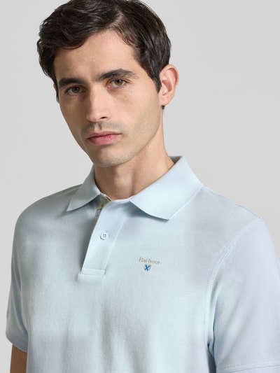 Männermodel trägt Regular Fit Poloshirt aus reine katoen van Barbour in effen kleuren met labelstitching, piqué structuur, polokraag, 2-knoopsluiting en korte mouw, detailaufnahme bovenlichaam.