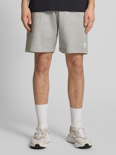 Männermodel trägt Regular Fit Sweatpants mit Logo-Stitching von adidas Originals in Grau, Baumwoll-Mix, Knielänge, Nahaufnahme Vorderansicht.