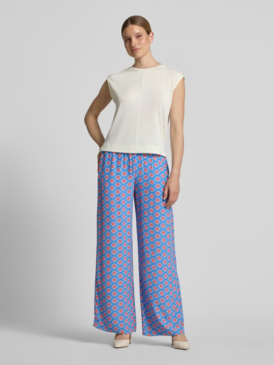 Frauenmodel trägt Wide Fit Stoffhose aus reiner Viskose mit Allover Motiv-Print von Smith and Soul in Blau und Rot, elastischer Bund, Ganzkörperansicht von vorne.