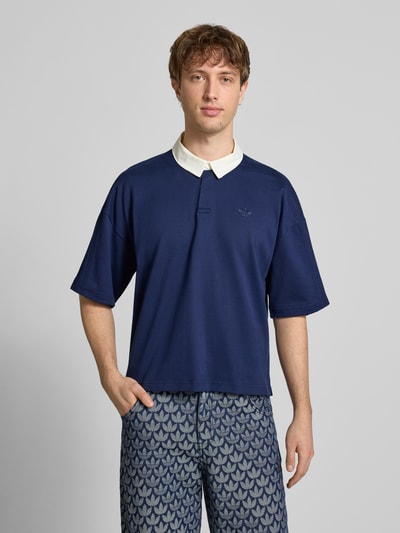 Männermodel trägt Regular Fit T-Shirt aus reiner Baumwolle von adidas Originals in Dunkelblau mit Polo-Kragen und Logo-Stitching, Ganzkörperansicht von vorne.