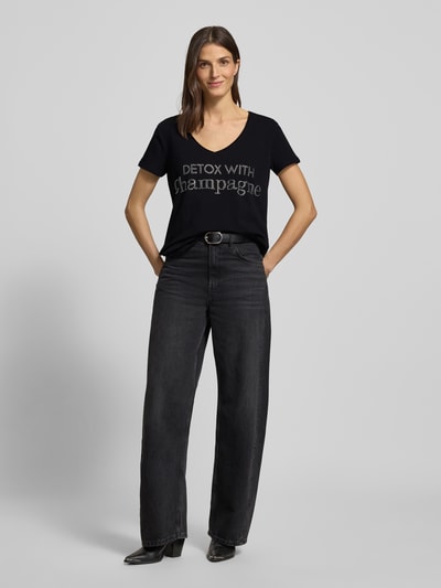 Vrouwenmodel draagt T-Shirt met Label-Detail van miss goodlife in zwart met V-hals, katoen-elastaanmix, losse pasvorm, voorkant volledig zichtbaar, Ganzkörperansicht von vorne.