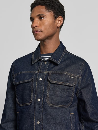 Męski model nosi Slim Fit Jeansjacke aus Baumwoll-Mix od Antony Morato, ciemnoniebieska, mieszanka bawełny i elastanu, wpuszczane kieszenie, listwa z zatrzaskami, wykładany kołnierz, szerokość ramion w rozmiarze 50: 42 cm, długość tyłu: 67 cm, szerokość w rozmiarze 50: 55 cm, długość rękawów: 67 cm, półzbliżenie przód.