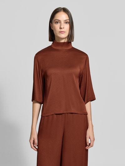 Frauenmodel trägt Regular Fit Bluse mit Stehkragen Modell 'Aletia' von DRYKORN, brauner elastischer Acetat-Mix, glatte Oberfläche, Ganzkörperansicht von vorne.