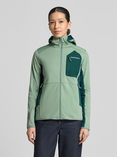Frauenmodel trägt Jacke mit Logo-Stitching von PEAK PERFORMANCE aus Elastischer-Material-Mix, körpernahe Passform, Kapuze, Reißverschluss, Brusttasche mit Reißverschluss, Ganzkörperansicht von vorne.