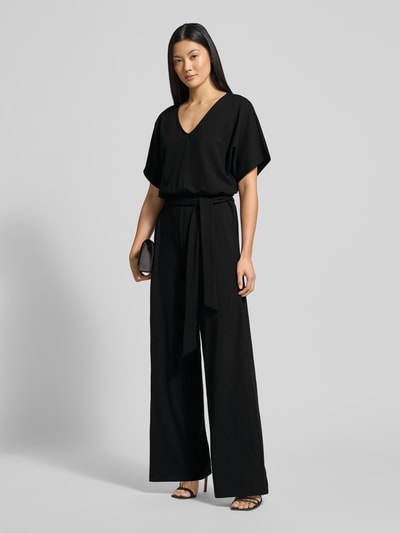 Frauenmodel trägt Jumpsuit mit Bindegürtel Modell 'Renata' von GUIDO MARIA KRETSCHMER WOMAN, schwarz, V-Ausschnitt, Ganzkörperansicht von vorne.