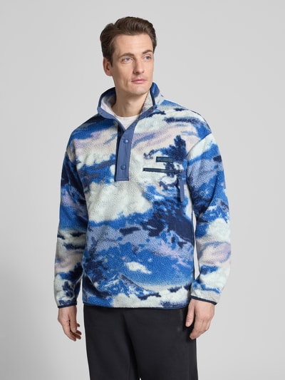Männermodel trägt Regular Fit Pullover mit Logo-Patch von Columbia in blauer Fließ-Optik, Brusttasche mit Reißverschluss, Ganzkörperansicht von vorne.