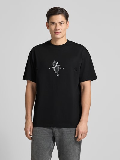 Männermodel trägt Regular Fit T-Shirt aus reiner Baumwolle Modell 'DOLLO' von HUGO, schwarz, grafisches Muster, Rundhals, Ganzkörperansicht von vorne.