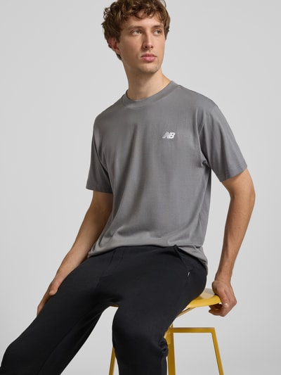 Männermodel trägt graues T-Shirt mit Logo und Rundhalsausschnitt von New Balance aus reiner Baumwolle, Regular Fit, Nahaufnahme Oberkörper.