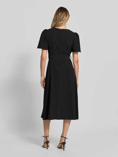 Frauenmodel trägt Cocktailkleid mit Gürtel und Rundhalsausschnitt von Rinascimento in Schwarz, Material-Mix mit Stretch-Anteil, Taillierter Schnitt, Midikleid, Rückseitiger Reißverschluss, Rückenlänge bei Größe S 36 cm, Brustweite 40 cm, Ärmellänge 28 cm, Ganzkörperansicht Rückansicht.