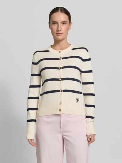 Frauenmodel trägt Regular Fit Strickjacke aus reiner Baumwolle von Tommy Hilfiger, Optik:Allover-Muster, Gestreift, Logo-Stitching, Regular-Fit, Knopfleiste, Rundhals, Langarm, Ärmelabschluss und Rumpfabschluss Gerippt, Feinstrick, Material: Reine Baumwolle, in hellen Farben mit navyfarbenen Streifen, glatte Textur, Ganzkörperansicht von vorne.