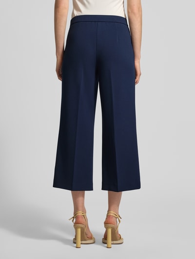Frauenmodel trägt Hose mit verkürzter Passform Modell 'Hillda-650' von STEHMANN aus dunkelblauem Material-Mix mit Stretch-Anteil, Bügelfalten, Ganzkörperansicht Rückansicht.