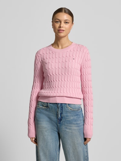 Modelka nosi Slim Fit Strickpullover aus reiner Baumwolle od Tommy Hilfiger, różowy, dzianinowy, krój slim fit, logo, długi rękaw, widok na całą sylwetkę z przodu.