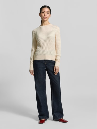 Frauenmodel trägt Slim Fit Pullover aus reiner Baumwolle von Tommy Hilfiger, Optik: Unifarben, Strickoptik, Zopfmuster, Logo-Detail, Rundhals, Langarm, Ärmelabschluss gerippt, Rumpfabschluss gerippt, Materialverarbeitung: Strick, Material: reine Baumwolle, Ganzkörperansicht von vorne.