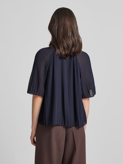 Frauenmodel trägt Regular Fit Blusenshirt in Plissee-Optik von s.Oliver BLACK LABEL, efekt: jednolity kolor, krój regular fit, kształt kołnierza: kołnierz z falbanami, detale: plisy, dekolt: okrągły dekolt, wycięcie w kształcie łezki, zapięcie: wiązanie, rękaw: krótki rękaw, tekstura lekko prześwitująca, kolor granatowy, Ganzkörperansicht Rückansicht.