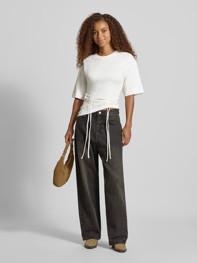 Kobiece modelka nosi damski t-shirt z bawełny, prosty krój, okrągły dekolt, marszczenia z wiązaniem, model 'MALLE' od Topshop, długość tyłu 66 cm w rozmiarze S, kolor biały, tekstura gładka, widok całej sylwetki z przodu.