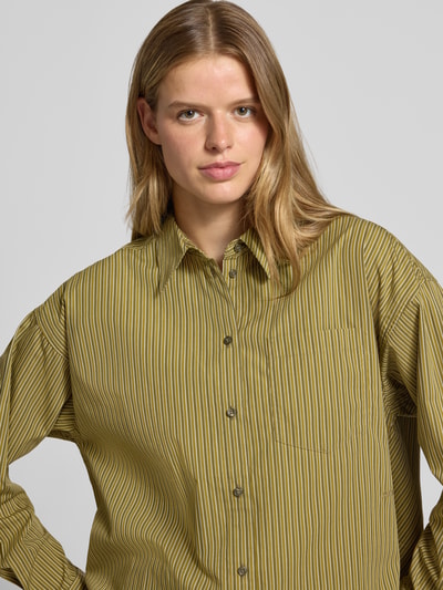 Frauenmodel trägt Relaxed Fit Hemdbluse aus reiner Baumwolle Modell 'JAMIE' von JJXX, gestreiftes Muster in Grüntönen, Nahaufnahme Oberkörper.