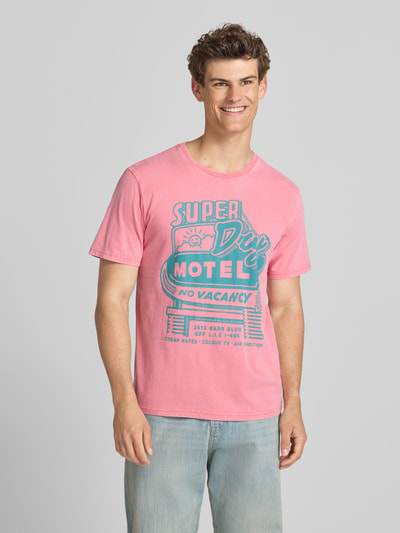 Männermodel trägt Loose Fit T-Shirt mit Label-Print Modell 'Roadside Trade' von Superdry in Rosa und Blau, reine Baumwolle, Ganzkörperansicht von vorne.