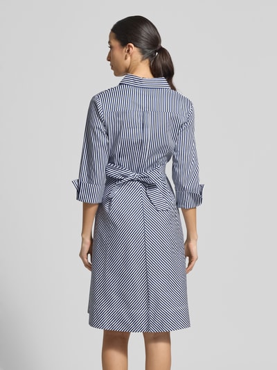 Modelka nosi Hemdblusenkleid mit Taillenband od Apricot w granatowo-białe paski, bawełna z domieszką elastanu, krój slim fit, długość midi, kołnierzyk kent, pasek w talii, rękawy 3/4, długość tyłu w rozmiarze S: 110 cm, szerokość w rozmiarze S: 40 cm, długość rękawa w rozmiarze S: 50 cm, widok całej sylwetki z tyłu.