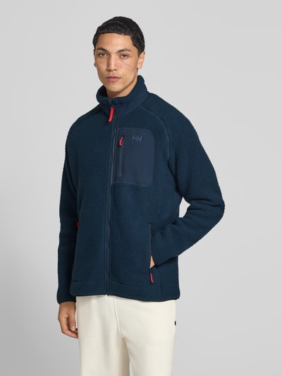 Männermodel trägt Fleecejacke mit Stehkragen von Helly Hansen in Dunkelblau, lockere Passform, Eingrifftaschen, Ganzkörperansicht von vorne.