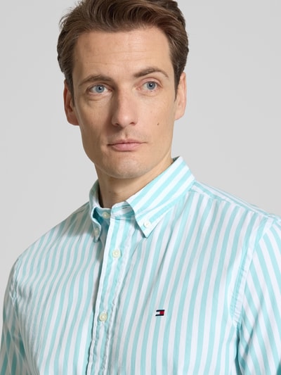 Männermodel trägt Regular Fit Freizeithemd aus Baumwoll-Popeline von Tommy Hilfiger, gestreiftes Muster in Türkis und Weiß, Nahaufnahme Oberkörper.