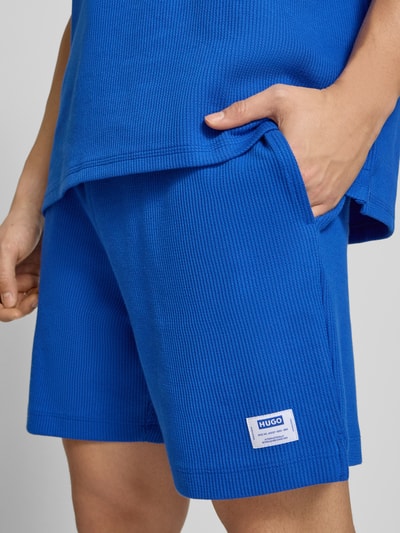 Männermodel trägt Regular Fit Sweatshorts aus Baumwoll-Mix Modell 'NUWAFFLO' von HUGO, Optik: Unifarben, Label-Patch, Nahaufnahme Oberschenkel.