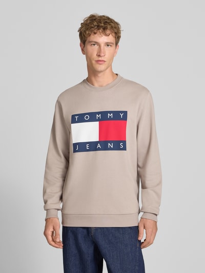 Męski model nosi Regular Fit Sweatshirt aus reiner Baumwolle von Tommy Jeans, jasnobeżowa bluza, prosty krój, wyraźne logo, Ganzkörperansicht von vorne