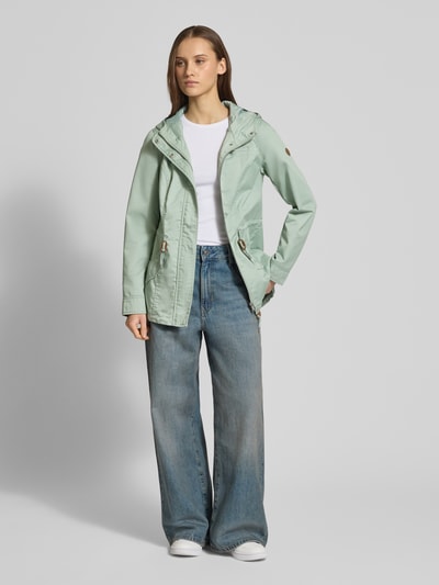 Modelka kobieca nosi Regular Fit Parka mit Baumwoll-Anteil Modell 'LORCA' od Only w kolorze miętowym, krój regular fit, bawełniany canvas, kaptur, długie rękawy, tunel w pasie, kieszenie z patką, kieszeń na piersi, kryte zapięcie na guziki i zamek, łatka z logo; zdjęcie całej sylwetki od przodu.