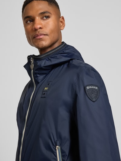 Männermodel trägt Jacke mit Label-Patches Modell 'Dodge' von Blauer Usa in Dunkelblau, Kapuze, Zweiwege-Reißverschluss, Nahaufnahme Oberkörper.