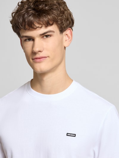 Männermodel trägt weißes Basic T-Shirt mit kleinem Logo-Patch auf der Brust von REVIEW, reine Baumwolle, Nahaufnahme Oberkörper.