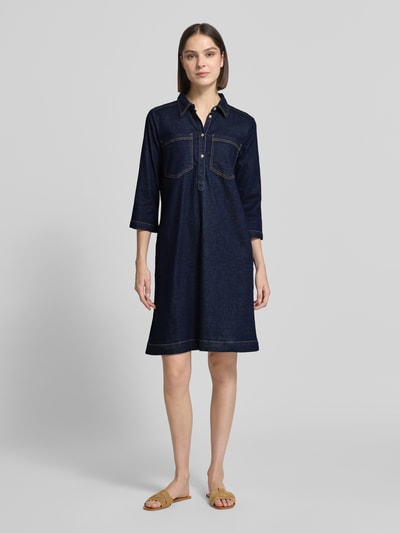 Vrouwenmodel draagt Regular Fit Jeanskleid aus Baumwoll-Mix van Tom Tailor in denimlook, knielang, hooggesloten hals, labelpatch, motiefstitching, knoopsluiting, 3/4-mouw, borstzakken, zijsteekzakken, katoenmix. Volledige lichaamsfoto van voren.