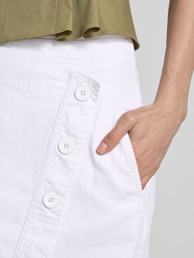 Kobieta nosi Straight Fit Midirock in Denim-Optik od Marc Cain, bawełniany materiał, białe guziki, kieszeń, surówkowa tekstura, zbliżenie na kieszeń. Szerokość w rozmiarze 36: 36 cm, długość całkowita: 90 cm.