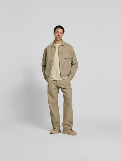 Männermodel trägt Jeansjacke aus Reiner Baumwolle von Forét in Beige, Regular-Fit, mit Durchgehender Knopfleiste, Brusttasche, Umlegekragen, Ganzkörperansicht von vorne.